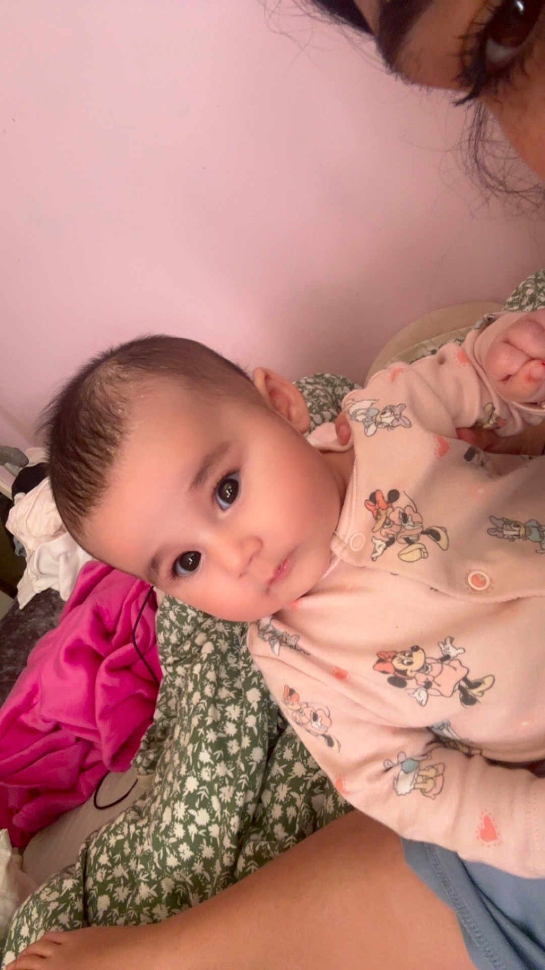 Amira is registered to the contest to win money with this photo: baby, child, infant, onesie, pink_clothing, cartoon_characters, face, eyes, skin, person, hand, blanket, fabric, bed, indoor, closeup, cute, soft_lighting, parent, holding
