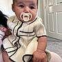 Amira is registered to the contest to win money with this photo: baby, pacifier, dress, knitwear, infant, child, person, indoor, carpet, door, hand, skin, cute, young, holding, sitting, apparel, fashion, portrait, curious