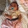 Amira joined the competition — help win amazing prizes! baby, pacifier, blanket, stuffed_animal, pink_cloth, clothing, infant, face, lying_down, cute, child, soft_toy, fabric, wearing, indoors, person, bed, comfort, fashion, adorable