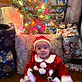 baby, celebration, child, christmas, costume, cute, decorations, festive, fur_trim, gift_wrap, holiday, indoor, lights, pillow, presents, red, santa_claus, smile, tree, white