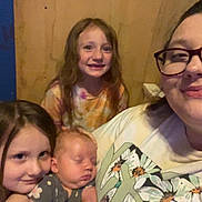 Ivy is registered to the contest to win money with this photo: woman, baby, child, glasses, smile, sleeping, indoor, bed, wooden_wall, blue_wall, person, family, casual_clothing, portrait, happy, young_girls, holding, closeup, together, home