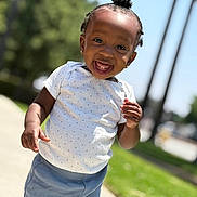 Cali is registered to the contest to win money with this photo: toddler, child, smiling, happy, outdoor, daylight, grass, trees, pants, shirt, polka_dot, hairstyle, top_knot, person, portrait, standing, sidewalk, sunlight, cute, young_child