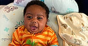 Kyzon is registered to the contest to win money with this photo: baby, infant, child, smiling, happy, portrait, lying_down, blanket, blue_blanket, orange_clothing, striped_clothing, cushion, bedding, indoors, home, nursery, patterned_fabric, dark_hair, open_mouth, cozy