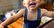 Hayes joined the competition — help win amazing prizes! baby, child, close_up, clothing, colorful, face, furniture, happy, home, indoor, laughing, overalls, play_area, portrait, sitting, smiling, standing, teeth, toddler, wood