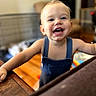 Hayes joined the competition — help win amazing prizes! baby, child, toddler, smiling, laughing, face, teeth, portrait, indoor, home, overalls, clothing, sitting, standing, furniture, wood, play_area, colorful, happy, close_up