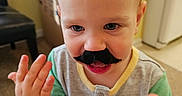 Hayes joined the competition — help win amazing prizes! toddler, child, baby, portrait, smiling, mustache, costume, funny, indoor, home, close_up, face, eyes, blond_hair, hands, waving, shirt, green_sleeves, adult_hand, carpet