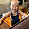 toddler, child, smiling, portrait, indoors, overalls, denim, blue_eyes, blond_hair, baby, standing, happy, face, arms, home, living_room, furniture, table, natural_light, photography