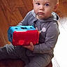 baby, child, toddler, sitting, toy, colorful_toy, red, blue, gray_clothing, wooden_floor, indoors, portrait, face, eyes, serious, looking_at_camera, bald, infant, playtime, home