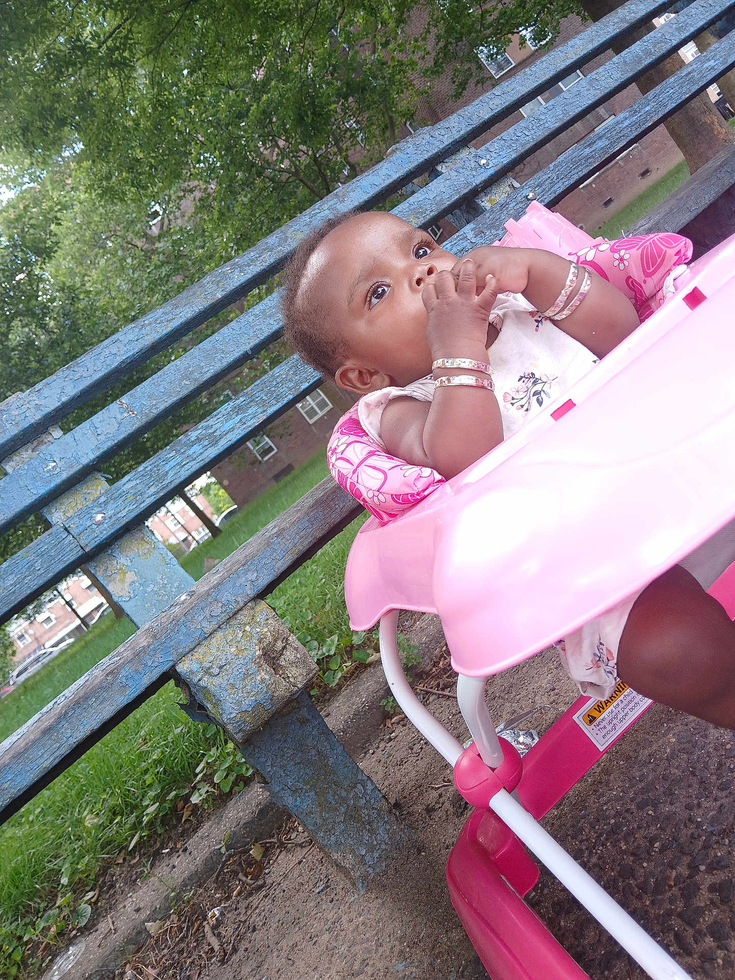 Faith is registered to the contest to win money with this photo: baby, child, walker, pink, outdoor, park, bench, greenery, curious, thoughtful, bracelet, grass, trees, sidewalk, building, daytime, person, infant, seat, playtime