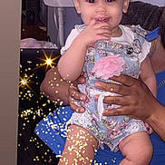 Kynzlee is registered to the contest to win money with this photo: baby, child, smiling, romper, bow, white_shoes, hand, adult, confetti, sparkles, indoor, person, cute, playful, sitting, holding, happy, face, legs, fashion