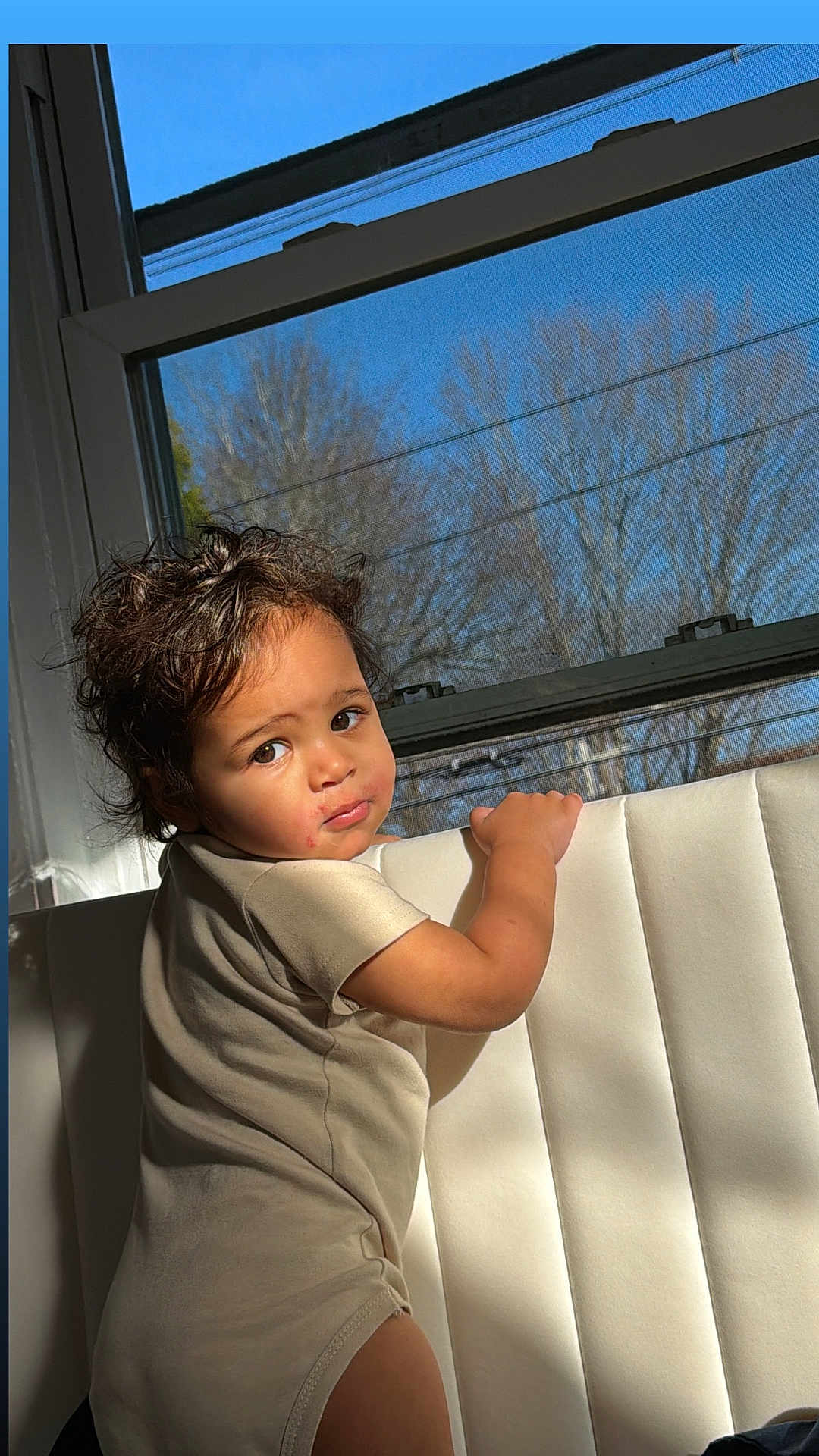Benício joined the competition — help win amazing prizes! child, toddler, baby, face, curly_hair, onesie, window, sunlight, shadow, indoor, upholstery, looking_back, portrait, cheeks, expression, arm, hand, daylight, home, seat
