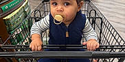 Benício joined the competition — help win amazing prizes! baby, toddler, child, pacifier, shopping_cart, supermarket, bananas, organic_section, navy_vest, striped_shirt, shoes, hands, face, eyes, sitting, grocery_shopping, aisle, wood_floor, groceries, portrait