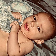 Alex joined the competition — help win amazing prizes! baby, infant, smile, face, hand, stuffed_animal, plush_toy, soft_texture, skin, lying_down, cute, child, portrait, closeup, indoors, comfort, joy, expression, toddler, warmth