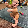 David is registered to the contest to win money with this photo: baby, child, infant, onesie, smiling, indoor, carpet, mat, toy, person, adult, blurred_background, playtime, crawling, happy, cute, floor, colorful, family, room