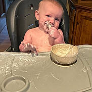 David is registered to the contest to win money with this photo: baby, highchair, messy, food, cream, bowl, indoor, child, smiling, face, hand, fingers, kitchen, wooden_cabinet, foot, table, feeding, happy, cute, infant