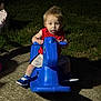 Coulson is registered to the contest to win money with this photo: toddler, child, blue_rocking_horse, outdoor, night, grass, sidewalk, red_shirt, white_shorts, blue_sneakers, toy, playground, grass_background, plastic_toy, footwear, person, young_child, cute, shadow, curious