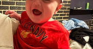 Zavier joined the competition — help win amazing prizes! baby, child, red_shirt, old_navy, hat, paper_hat, in_n_out_burger, smiling, happy, indoor, living_room, brick_wall, person, hand, holding, furniture, couch, clothing, casual, portrait