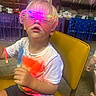 child, boy, glowing_glasses, yellow_chair, white_tshirt, paint_splatter, shorts, glow_bracelet, indoor, party, balloon, furniture, curious_expression, light_effects, face, person, seated, event, decorations, floor