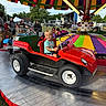 child, carnival, ride, mini_car, red, smile, outdoor, amusement_park, people, colorful, canopy, fun, summer, festival, happy, vehicle, toy_car, family, daytime, park