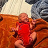 newborn, baby, infant, red_onesie, blanket, orange_blanket, blue_blanket, gray_blanket, sleeping, smiling, peaceful, sunlight, indoors, soft_texture, cozy, cute, skin, hand, foot, lying_down