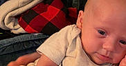 Raelynn is registered to the contest to win money with this photo: baby, infant, onesie, nike_logo, blanket, indoor, soft_fabric, plaid, red, white_clothing, child, person, skin, head, arm, hand, relaxed, couch, casual, home