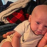 baby, infant, onesie, nike_logo, blanket, indoor, soft_fabric, plaid, red, white_clothing, child, person, skin, head, arm, hand, relaxed, couch, casual, home