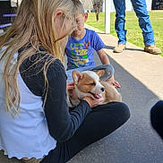 Rip is registered to the contest to win money with this photo: child, dog, puppy, outdoor, concrete, grass, person, blue_shirt, long_hair, jeans, boots, sitting, playing, sunny, happy, casual_clothing, daytime, pet, family, interaction