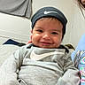 Luca is registered to the contest to win money with this photo: baby, child, smiling, person, indoor, clothing, hat, nike, gray, cute, portrait, face, hand, sitting, young, apparel, joyful, infant, holding, cozy
