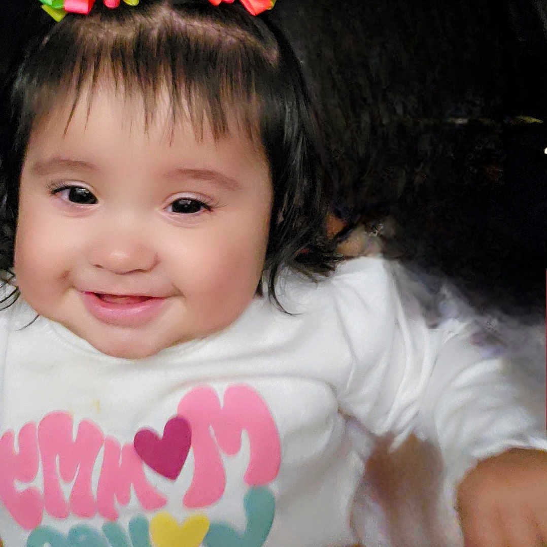 J'Lani joined the competition — help win amazing prizes! baby, child, chubby_cheeks, close_up, colorful, cute, dark_background, eyelashes, face, front_facing, hair_bows, happy, indoors, long_sleeve, person, portrait, smiling, text_on_shirt, toddler, white_shirt