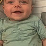 airplane_pattern, baby, blanket, child, close_up, clothing, couch, eyes, face, happy, home, indoors, infant, onesie, pajamas, portrait, reclining, sitting, smiling, vehicle_pattern