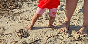 Aria is registered to the contest to win money with this photo: toddler, child, beach, sand, seaweed, bucket_hat, red_tshirt, pink_shorts, holding_hand, adult_legs, bare_feet, footprints, shoreline, sunny, outdoor, portrait, small_child, summer, walking, family