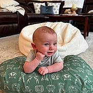 Isaac is registered to the contest to win money with this photo: baby, infant, cushion, green, pattern, smile, face, living_room, carpet, blanket, sofa, pillow, wooden_table, home_interior, cute, person, child, relaxed, bright, indoor