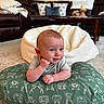baby, infant, cushion, green, pattern, smile, face, living_room, carpet, blanket, sofa, pillow, wooden_table, home_interior, cute, person, child, relaxed, bright, indoor