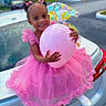 child, girl, balloon, pink_dress, hair_bows, smiling, car_trunk, outdoor, daylight, white_shoes, tulle, happy, celebration, person, vehicle, colorful, cute, fashion, joyful, portrait