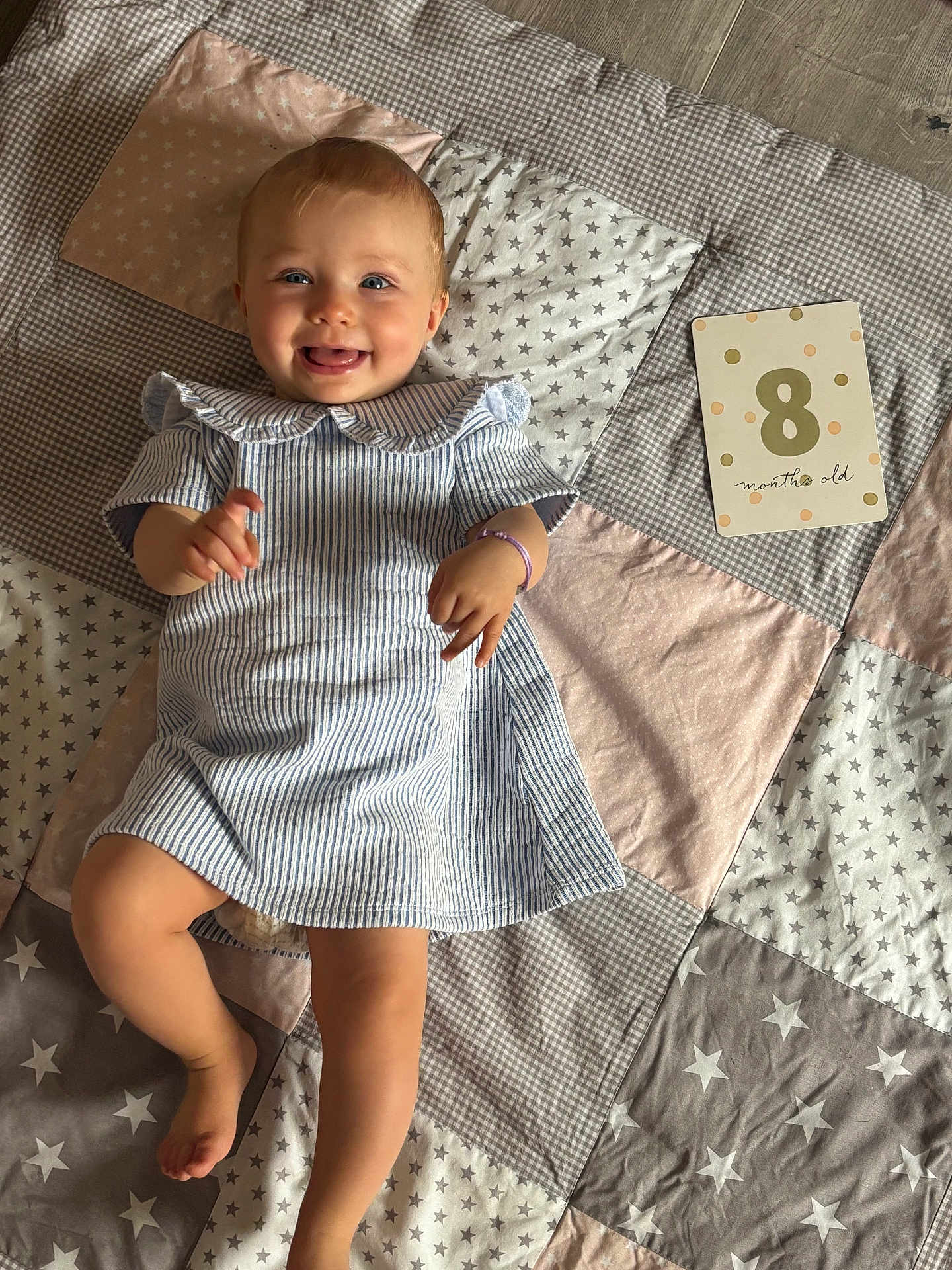 Albane participe au concours pour gagner de l'argent avec cette photo : baby, infant, child, smiling, striped_dress, blue_eyes, patchwork_quilt, star_pattern, pastel_colors, barefoot, card, 8_months_old, cute, happy, lying_down, soft_lighting, playful, ruffled_collar, bracelet, indoor