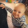Louise participe au concours pour gagner de l'argent avec cette photo : baby, child, smiling, striped_shirt, indoor, floor, toy, radiator, wooden_furniture, pink_baby_seat, black_jacket, person, hand, face, leg, sock, home, flooring, cute, happy