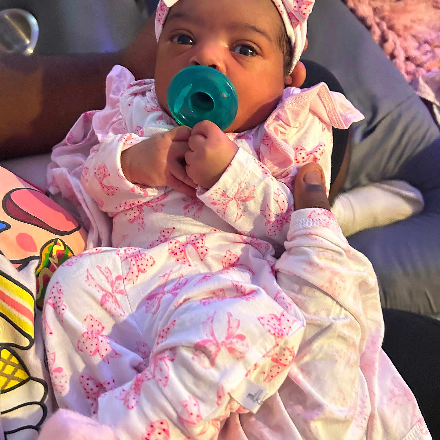 Raphinha is registered to the contest to win money with this photo: adult, baby, blanket, bow, clothing, cozy, cute, hand, headband, holding, indoors, infant, newborn, pacifier, pattern, person, pink, portrait, sleepwear, soft