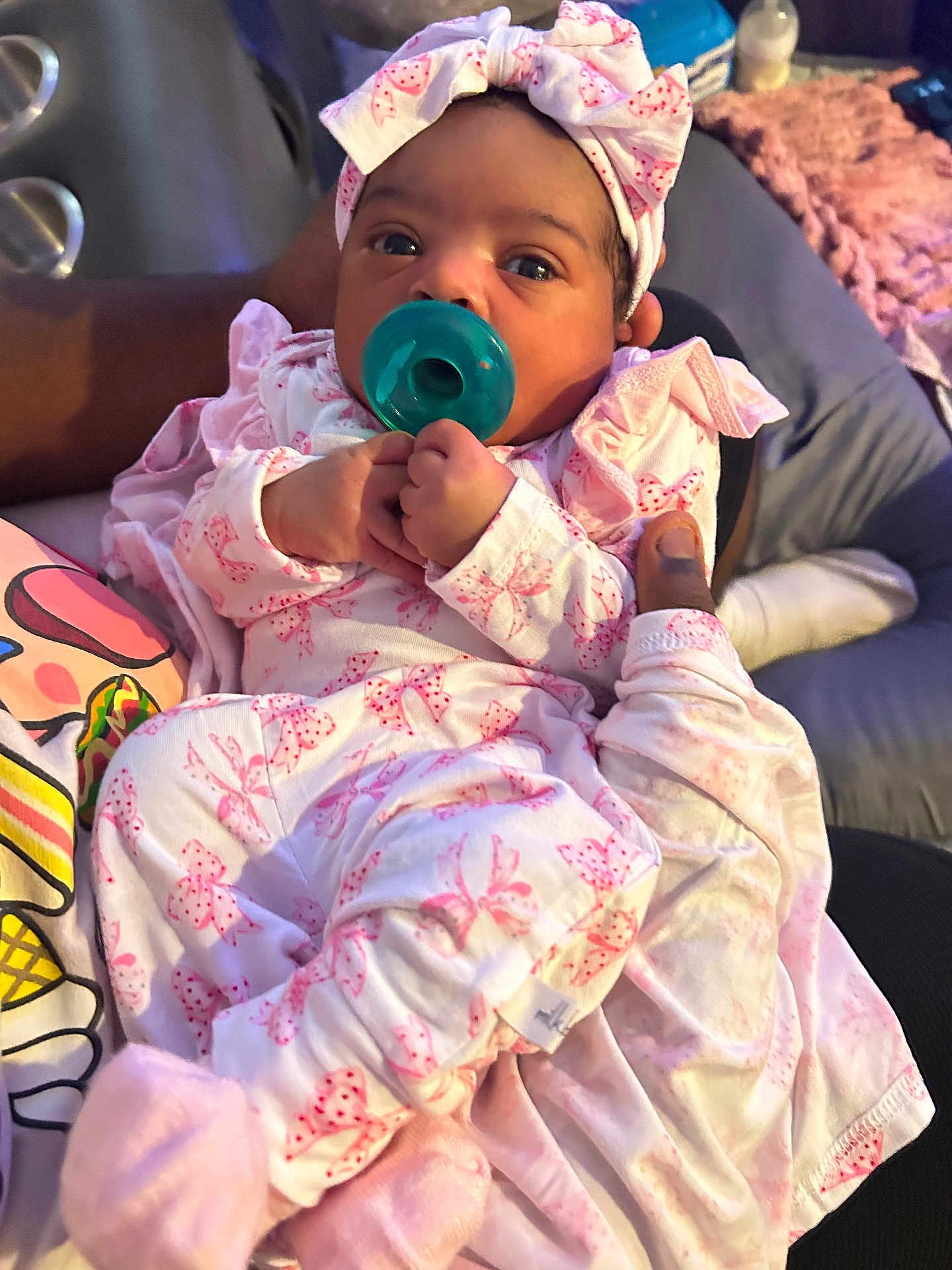 Raphinha is registered to the contest to win money with this photo: adult, baby, blanket, bow, clothing, cozy, cute, hand, headband, holding, indoors, infant, newborn, pacifier, pattern, person, pink, portrait, sleepwear, soft