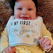 Lenora joined the competition — help win amazing prizes! baby, smiling, bib, black_bow, yellow_pajamas, plush_blanket, happy, infant, face, child, cute, new_years, portrait, clothing, hand, sitting, indoor, cozy, celebration, person