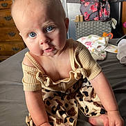 Huntleigh is registered to the contest to win money with this photo: baby, blue_eyes, clothing, curious, bed, indoor, infant, leopard_print, person, portrait, sitting, skin, soft_lighting, top, young_child, hand, foot, furniture, room, casual