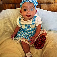 Lola is registered to the contest to win money with this photo: baby, child, blue_dress, headband, red_shoes, sitting, cushion, white_socks, wooden_background, indoor, cute, portrait, infant, clothing, fabric, face, expression, small_hands, furniture, person