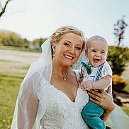 Elliot is registered to the contest to win money with this photo: bride, baby, wedding_dress, veil, outdoor, smile, happy, child, portrait, nature, grass, tree, person, celebration, event, holding, formal_wear, joy, family, daylight