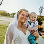 bride, baby, wedding_dress, veil, outdoor, smile, happy, child, portrait, nature, grass, tree, person, celebration, event, holding, formal_wear, joy, family, daylight