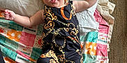 Kynslee joined the competition — help win amazing prizes! baby, child, headband, yellow_bow, black_outfit, patterned_clothing, blanket, colorful_blanket, text_on_blanket, happy, smiling, lying_down, carpet, indoors, cute, infant, person, fabric, playful, expression