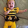 baby, child, infant, yellow, black, headband, bow, smile, happy, cute, lying_down, blanket, clothing, costume, bee, striped, pants, sleeves, feet, expression