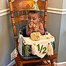 baby, birthday, cake, celebration, child, cute, decor, eating, face, flooring, food, green_wall, hands, high_chair, home_interior, infant, messy, party_hat, tassels, wooden_chair