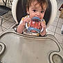 toddler, child, high_chair, sippy_cup, kitchen, tile_floor, table, chair, baby, person, drinking, plastic_cup, cute, indoor, young_child, feeding_time, face, hands, clothing, expression