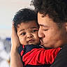 baby, child, infant, person, face, love, affection, family, cuddle, kiss, curly_hair, red_clothing, black_clothing, portrait, close_up, indoor, skin, young_adult, expression, bond