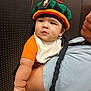baby, child, person, hat, knit_hat, orange_shirt, bib, braids, arm, adult, holding, curious, indoor, portrait, face, cute, chubby, black_hair, closeup, background