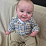 baby, child, infant, smiling, happy, portrait, sitting, couch, sofa, blanket, plaid_shirt, clothing, trousers, barefoot, face, eyes, hands, indoor, home, family